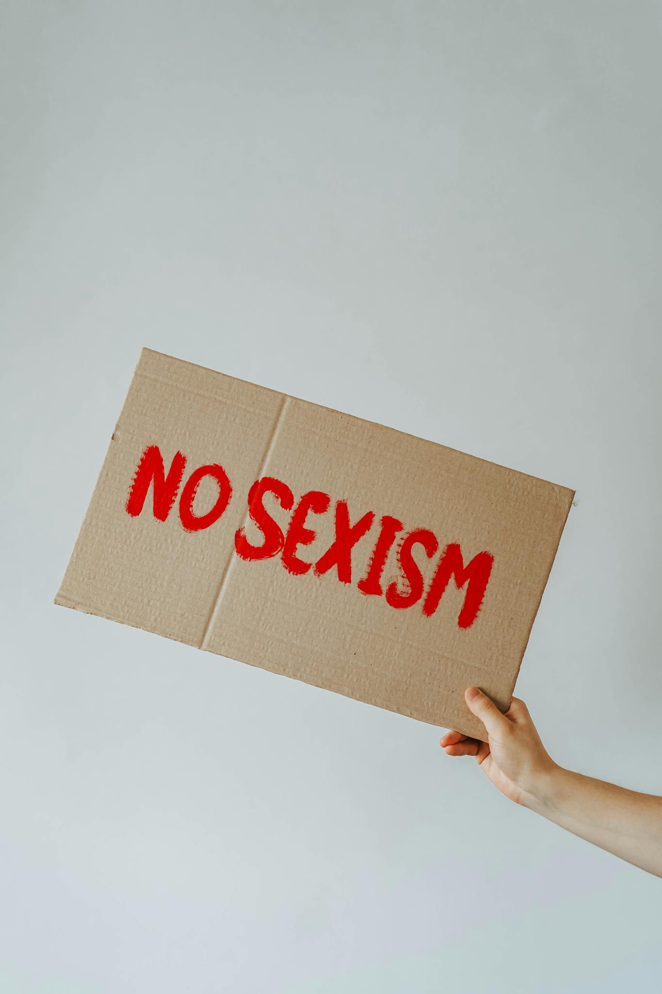 A powerful image of a cardboard sign with 'No Sexism' message, held by a hand.