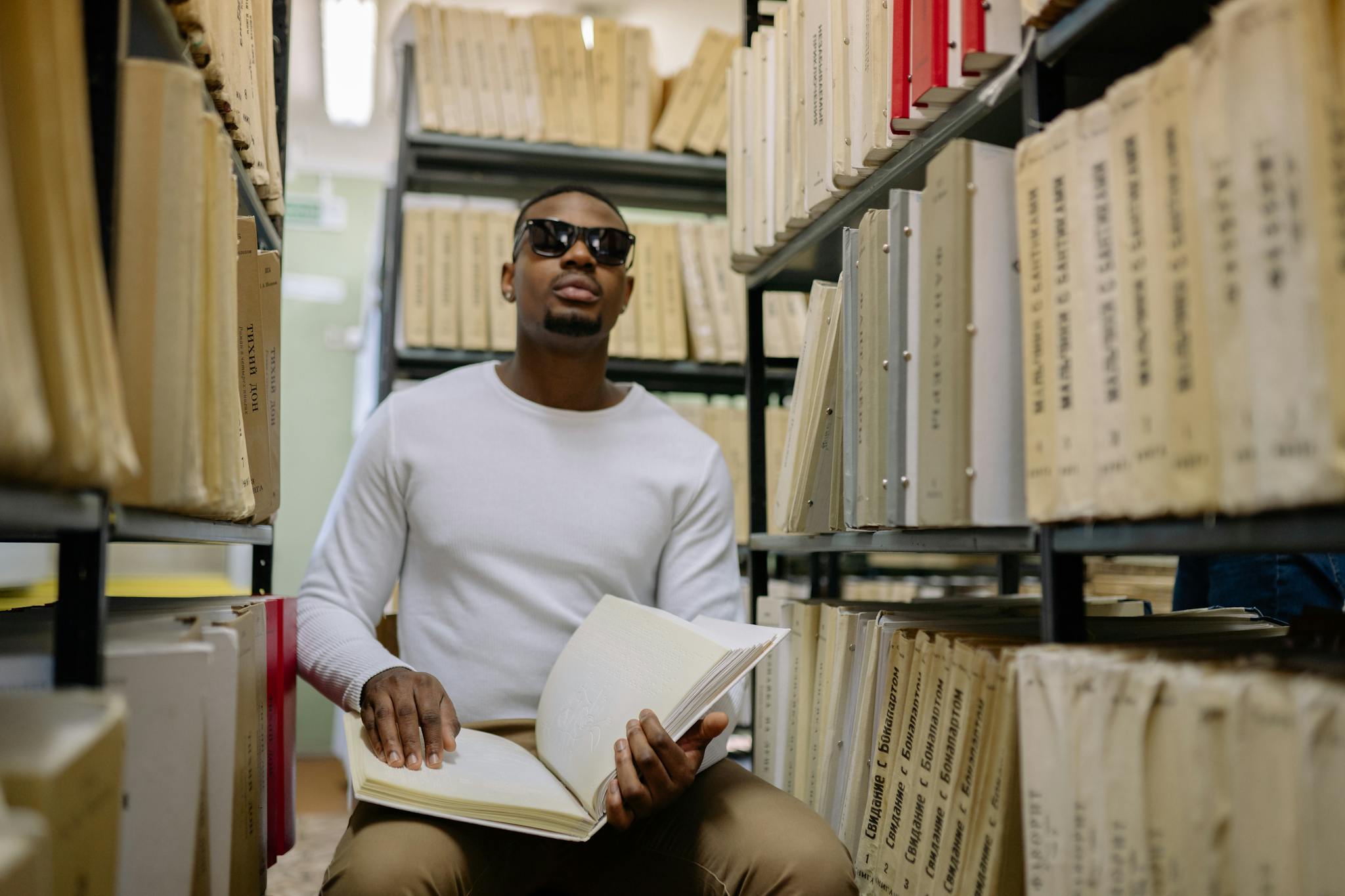 African American man with visual impairment reading braille book in a library.