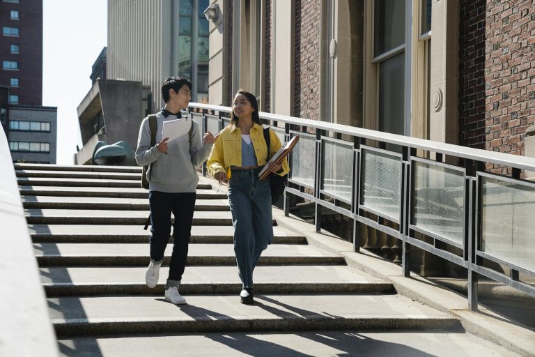 Two college students walking and conversing on a sunlit campus stairway.